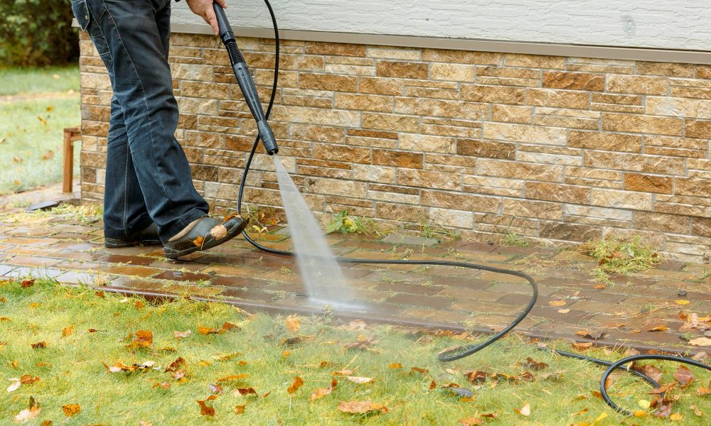 Man cleaning street with high pressure power washer, washing stone garden paths